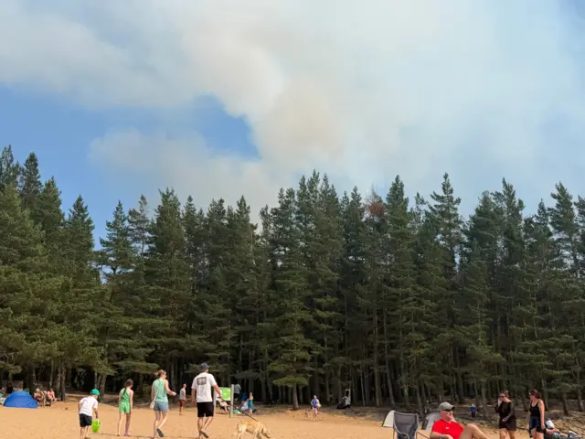 People on Loch Morlich beach, with smoke visible in the sky