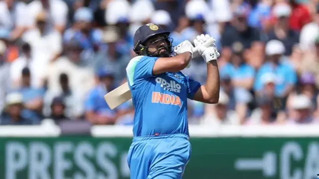 Rohit Sharma, wearing all blue with a dark blue helmet, with his bat behind his left shoulder in his follow-through