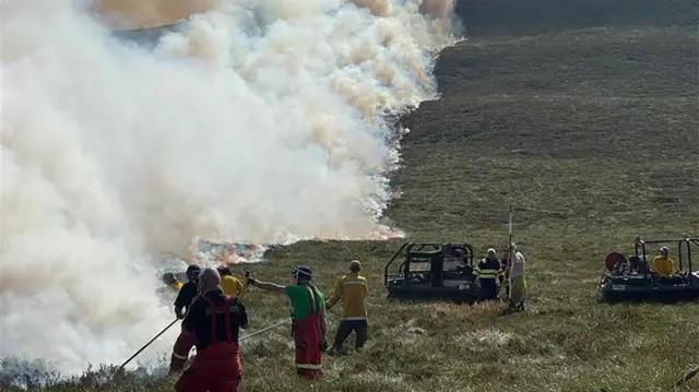 firefighters in overalls standing next to a large plume of smoke