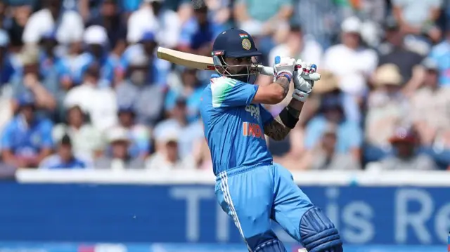 Virat Kohli, wearing all blue and a dark blue helmet, turns with his bat over his left shoulder in his follow through