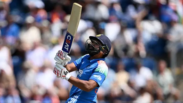 Rohit Sharma, wearing a blue India shirt and dark blue helmet, holds his bat high in front of him in two hands.