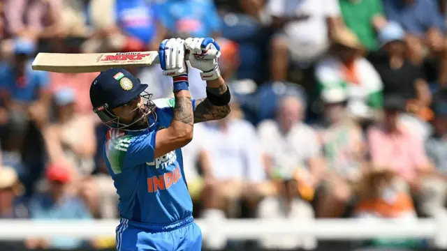 Virat Kohli, wearing a blue India kit and dark blue helmet, in his follow-through, with his bat held high to his left