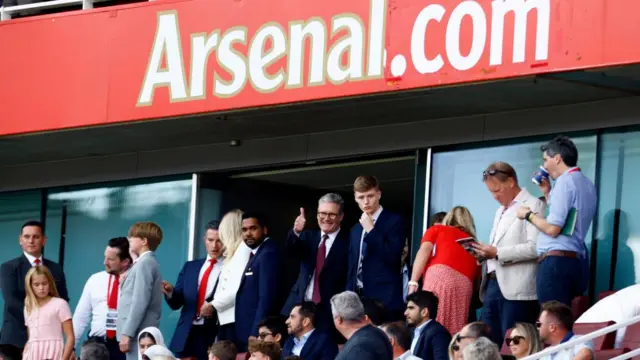 Keir Starmer among a crowd of people underneath a sign reading Arsenal.com