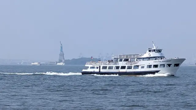 A ship moves towards the right of frame with hazy view of the Statue of Liberty in the background.