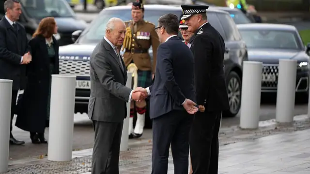 King Charles III and Andy Burnham shaking hands, two police officers stand nearby