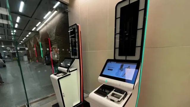 Two white machines with screens and a all array of cameras. One has green lights and the other has red lights.