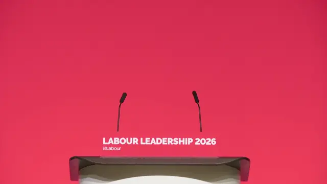 an empty lectern standing in front of a red wall