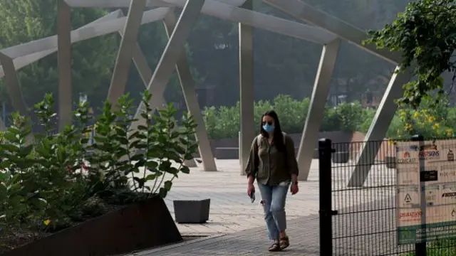 A woman walks through a park with a blue facemask on