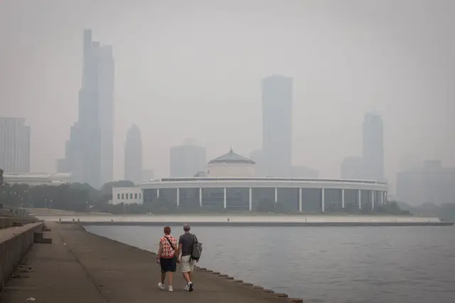 Man and woman in shorts and short-sleeved shirts with lake water to their right and a hazy skyline in front of them