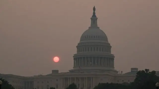 The sun rises behind the US Capitol building as smoke hangs in the air