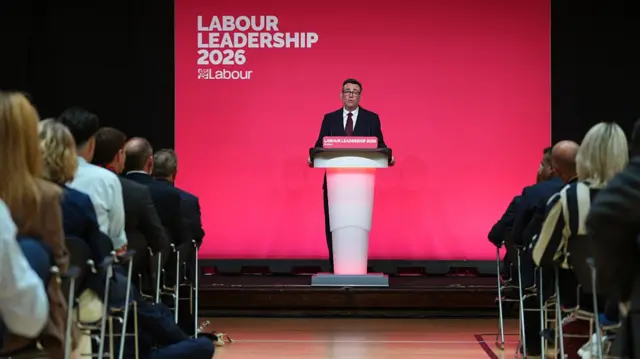 Burnham speaking at the podium in front of an audience