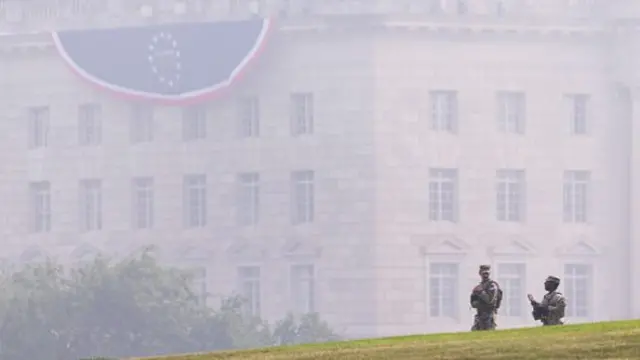 Army National Guard members patrol in front of the Herbert C. Hoover Federal Building shrouded in smoke