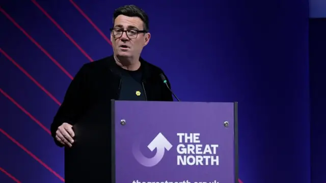 Andy Burnham pictured behind a purple lectern that says 'The Great North'