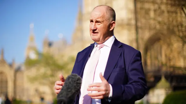 Kevin Hollinrake speaks to a microphone while standing outside the House of Parliament in Westminster, London