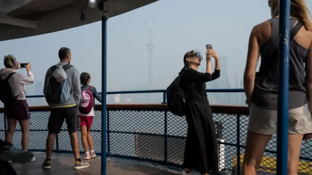 Tourists look at a hazy downtown Toronto skyline from a ferry crossing Lake Ontario, Toronto, Ontario, Canada, 16 July 2026