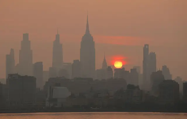 The sun rises behind the midtown Manhattan skyline and Empire State Building, casting the city in an orange haze