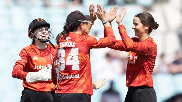 Charli Knott high fives with teammates after taking a Surrey wicket