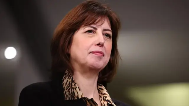 Lucy Powell wears a patterned collared shirt and a black cardigan, her brown hair is cut short in a bob.