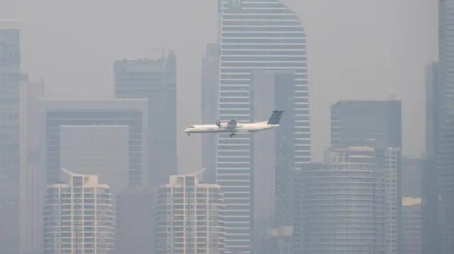 A plane flies past smog-covered Toronto high-rises