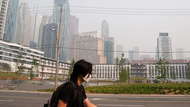 A man wearing face mask walks on the street as smoke from wildfires continue to impact air quality in Toronto, Ontario on July 16, 2026