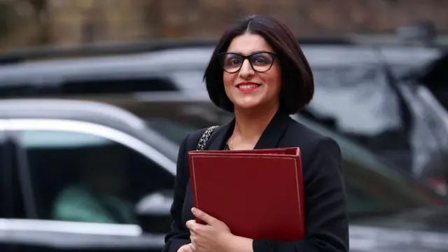 Shabana Mahmood walking with her red binder in hand and smiling