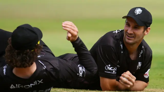 Lewis Gregory has the ball in his left hand as he smiles at Tom Kohler-Cadmore with both of them lying on the ground