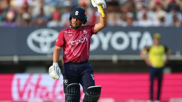 Ricardo Vasconcelos raises his bat after scoring fifty