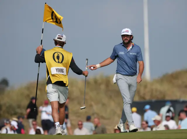 Cameron Young looking frustrated as he passes his putter to his caddie