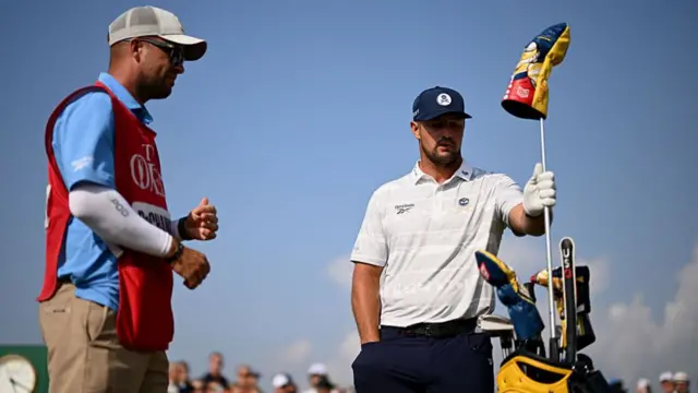 Bryson DeChambeau holds a flag next to his caddie
