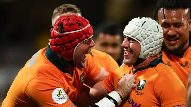 Josh Canham (right), wearing a white scrum cap and yellow Australia shirt, celebrates with teammates