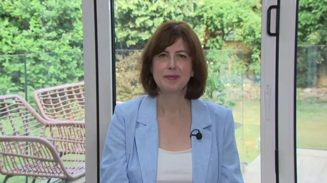 Lucy Powell, a woman sitting in a conservatory, wearing a blue blazer, with a microphone attached to her blazer.