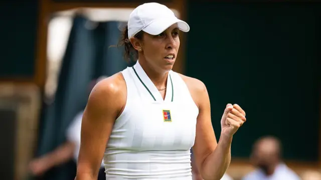 Madison Keys, wearing a white sleeveless dress and white cap, clenches her left fist