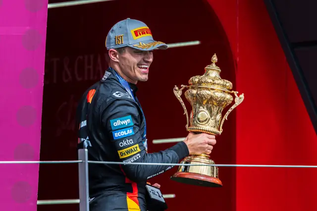 Lando Norris holds the British GP winner's trophy on the podium at Silverstone