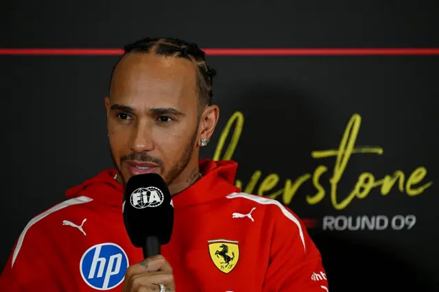 Lewis Hamilton holds a microphone while answering questions in the news conference at Silverstone