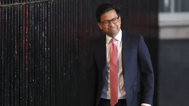 Kanishka Narayan MP walking into Downing Street, wearing a salmon-white checkered tie and navy jacket. He wears round frames.