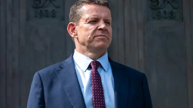 Rhun ap Iorwerth stood in front of a wooden door