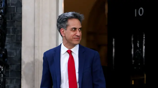 Ed Miliband in blue suit, red tie and white shirt walking out of No 10
