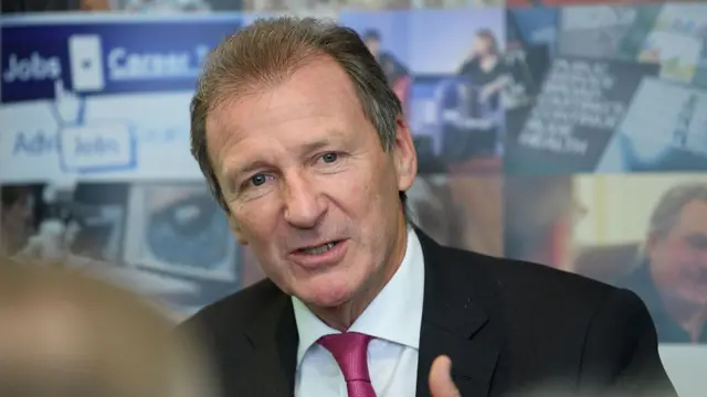 Gus O'Donnell - an older white man - in a black suit, white shirt and pink tie.