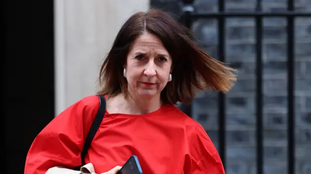 Liz Kendall in a red top walking away from No 10 while holding a phone in her right hand