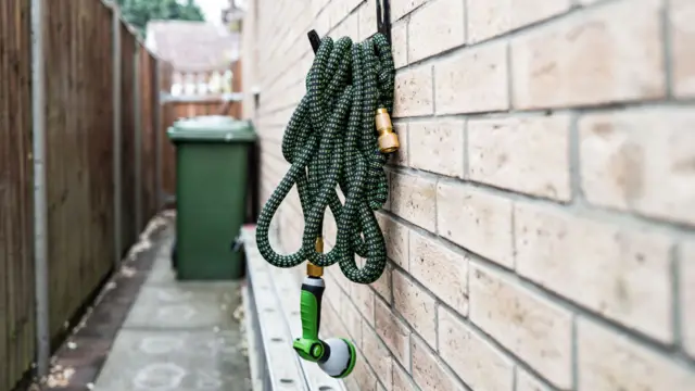 A hosepipe wrapped up and placed on a hook on the outside of a brick house.