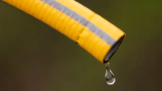A yellow hosepipe with a water drop coming from it.
