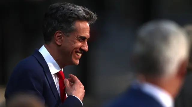 Miliband, who has greying dark hair, beams as he stands outside No 10 in a navy suit, white shirt and red tie