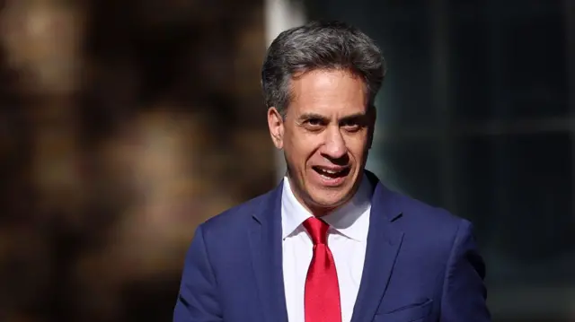 Ed Miliband in dark blue suit, red tie and white shirt mid-speech as he walks towards No 10