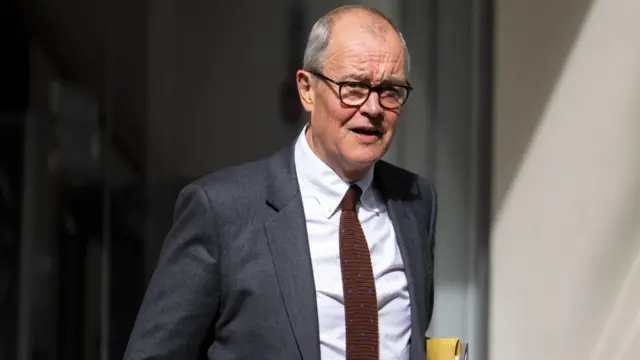 Lord Vallance leaving a building, carrying a pile of papaerwork