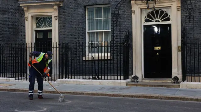 A street cleaner sweeps the road outside 10 Downing Street