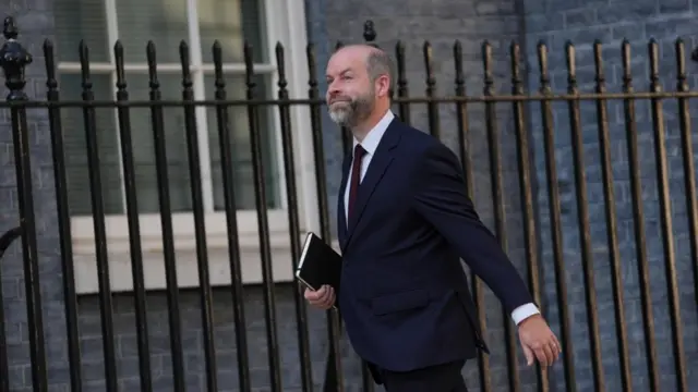 Reynolds walks in front of a fence smiling holding a black book