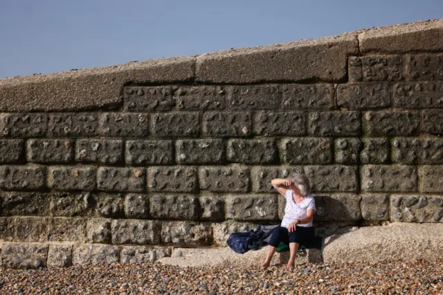 A woman shielding her eyes from the son and looking out at the sea.