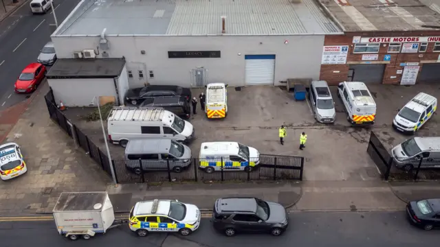 Aerial view of the Legacy funeral home in Hull a grey industrial unit with a car park at the front. A number of police cars and police officers are outside.