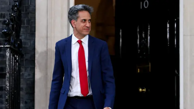 Ed Miliband, wearing a navy suit, white shirt and red tie, walking out of No 10 Downing Street
