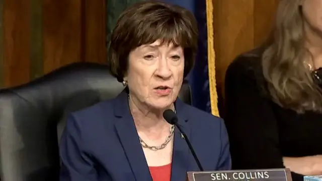 Collins speaking into a small mic propped up on a desk in front of her while she is sitting in a black leather chair